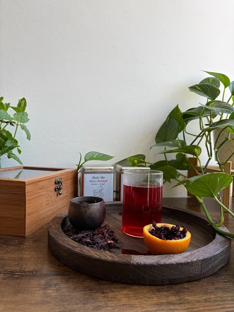 Deep ruby-red hibiscus tea brewed in a glass cup beside dried hibiscus calyces