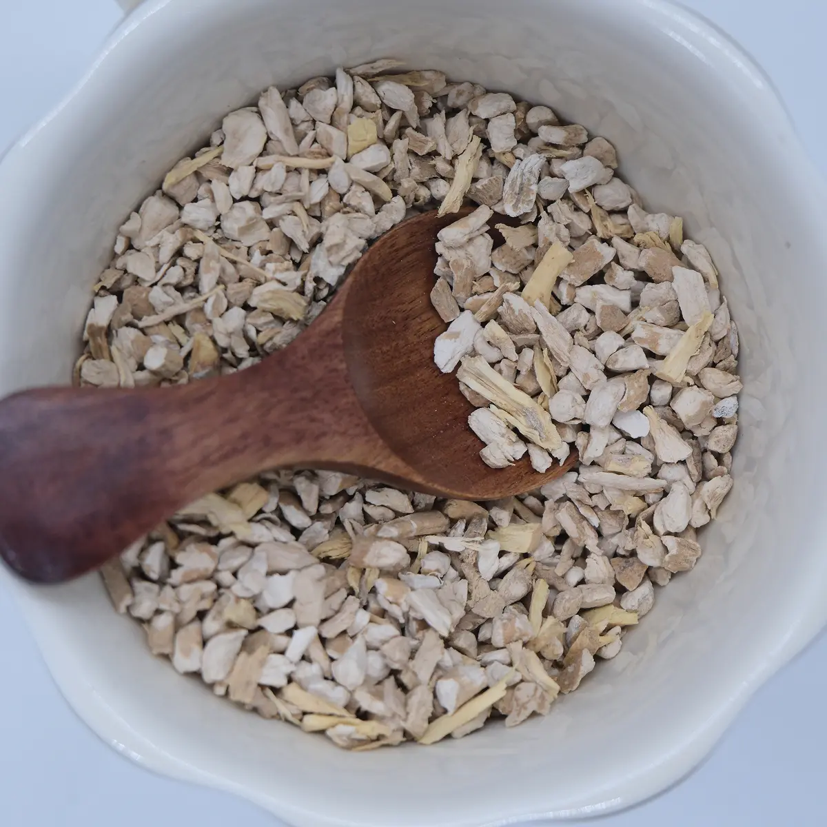 Cut ashwagandha root in a white bowl with a wooden scoop