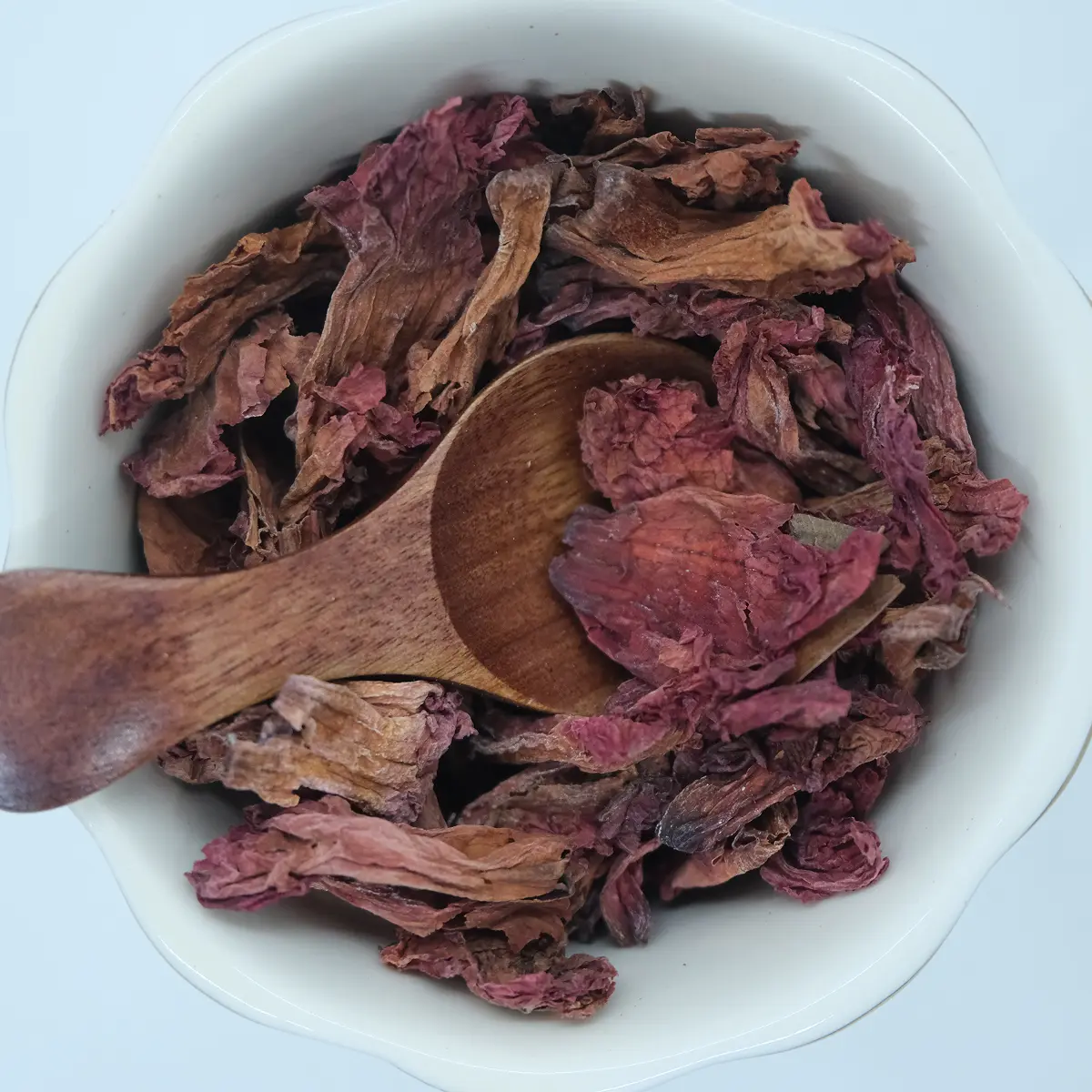 Dried rhododendron petals in a white bowl with a wooden scoop