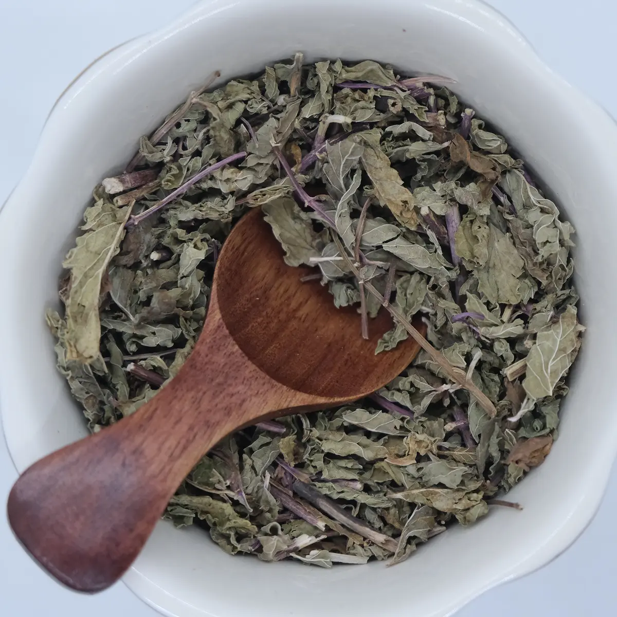 Dried spearmint leaves in a white bowl with a wooden scoop